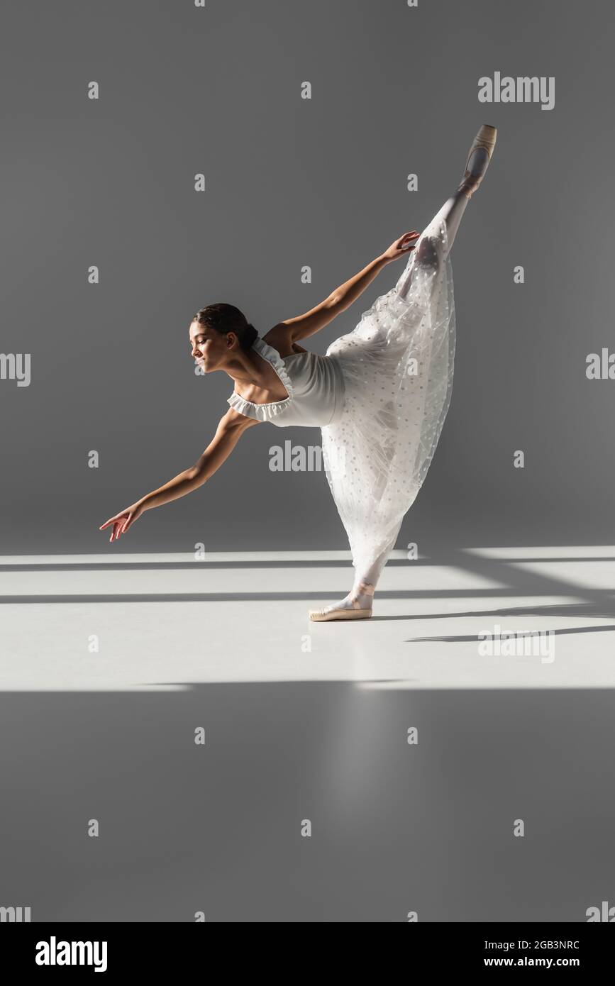 Seitenansicht der Ballerina, die auf einem Bein auf grauem Hintergrund steht Stockfoto