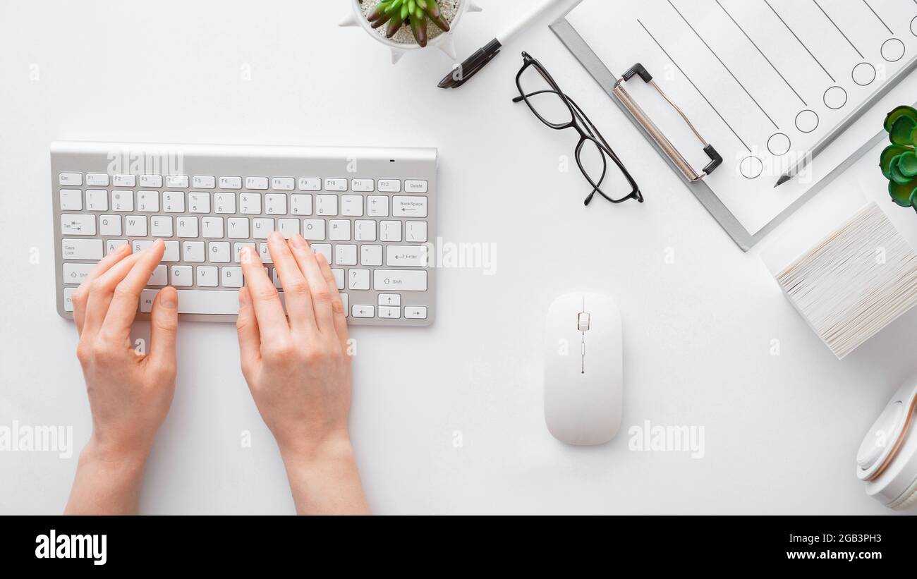 Weibliche Hände tippen auf der Tastatur am Büroarbeitsplatz am weißen Tisch. Flach Lay Frau Hände auf weißen Tisch Schreibtisch verwenden pc-Computer. Draufsicht. Langes Webbanner Stockfoto
