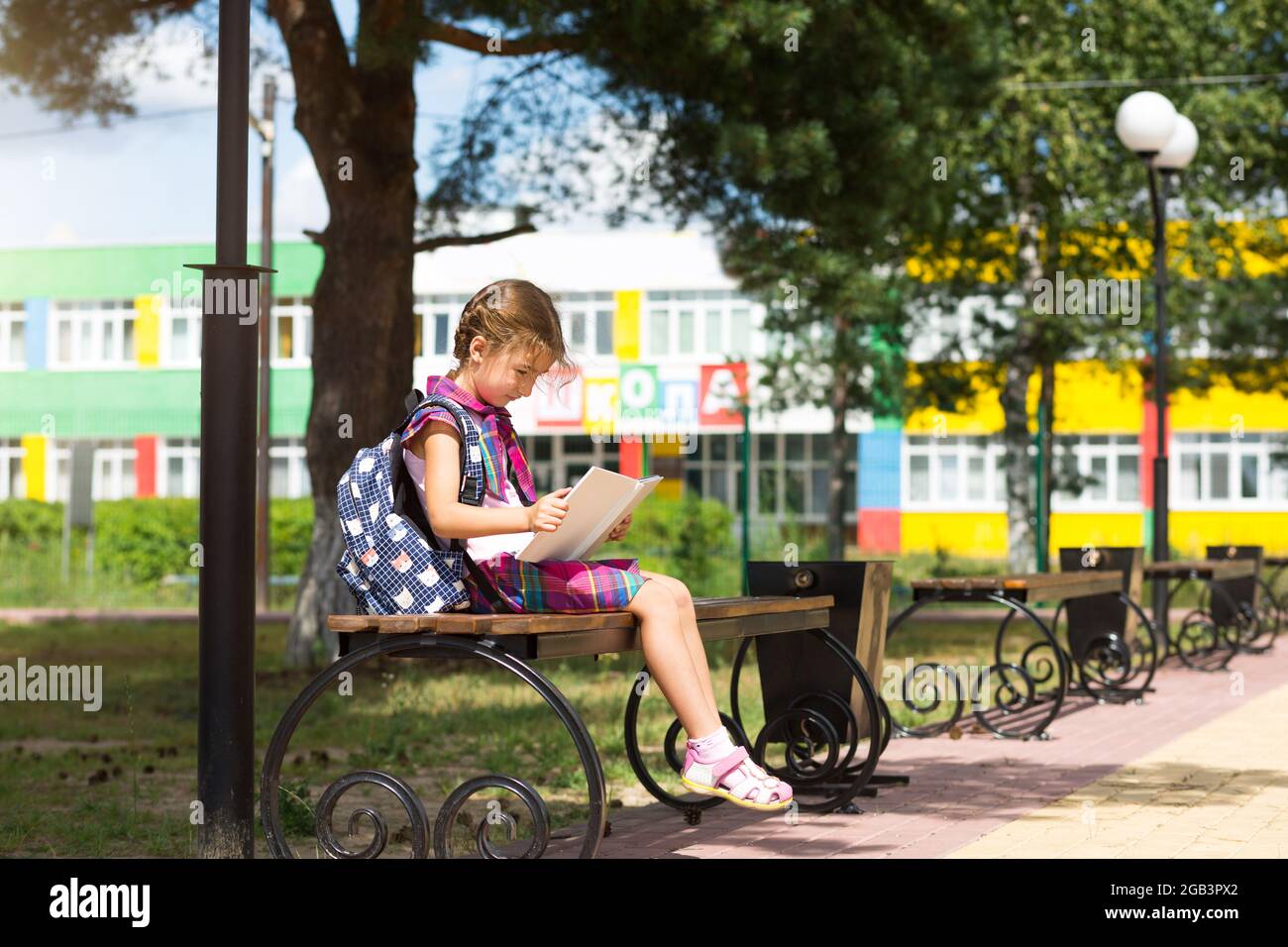 Mädchen mit Rucksack, das auf einer Bank sitzt und ein Buch in der Nähe der Schule liest. Zurück zur Schule, Stundenplan, ein Tagebuch mit Noten. September. Die ins Stockfoto