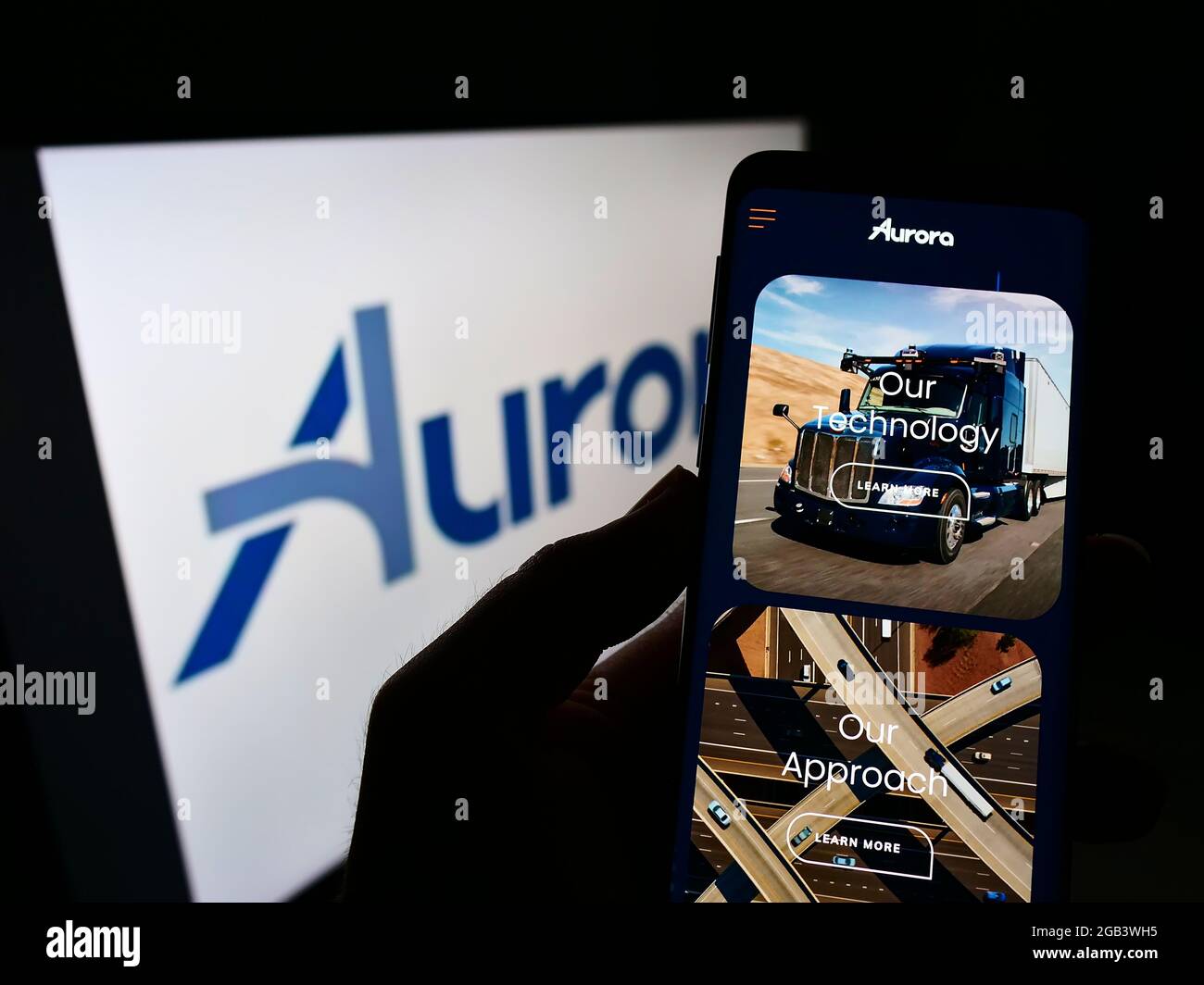 Person mit Mobiltelefon und Webseite des selbstfahrenden Fahrzeugunternehmens Aurora Innovation Inc. Auf dem Bildschirm mit Logo. Konzentrieren Sie sich auf die Mitte des Telefondisplays. Stockfoto