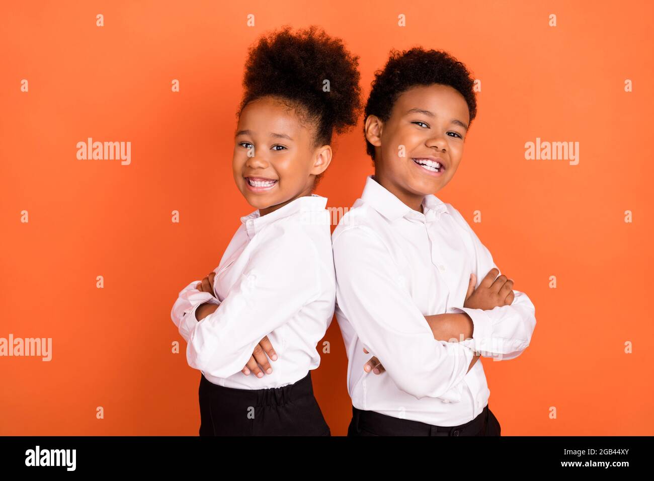 Profil Seitenfoto von zwei jungen schwarzen Kindern glücklich positive Lächeln Pupille uniform gekreuzte Hände isoliert über orange Farbe Hintergrund Stockfoto