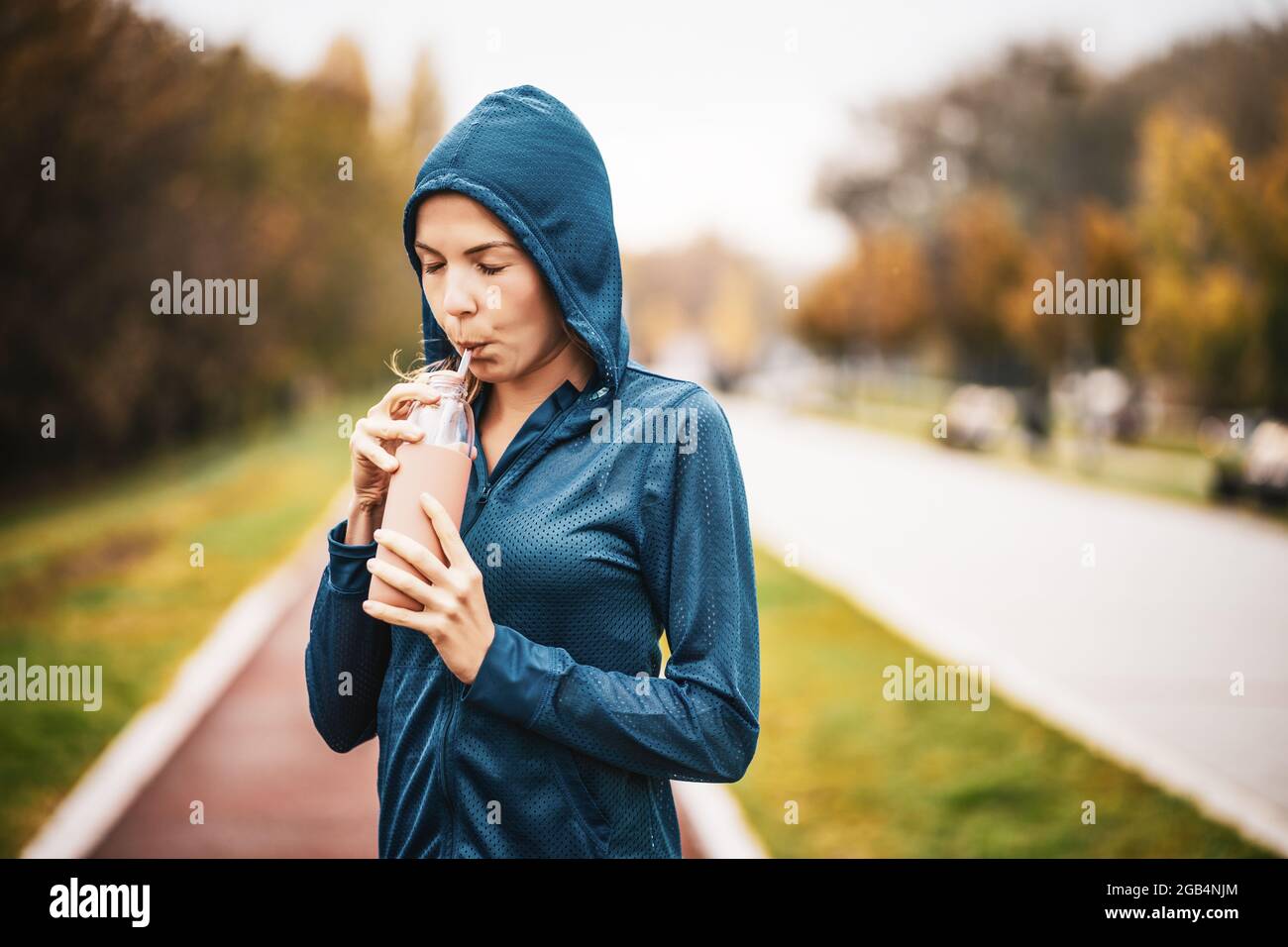 Erwachsene Frau trinkt Wasser, während sie an bewölktem Tag im Herbst im Freien trainiert. Stockfoto