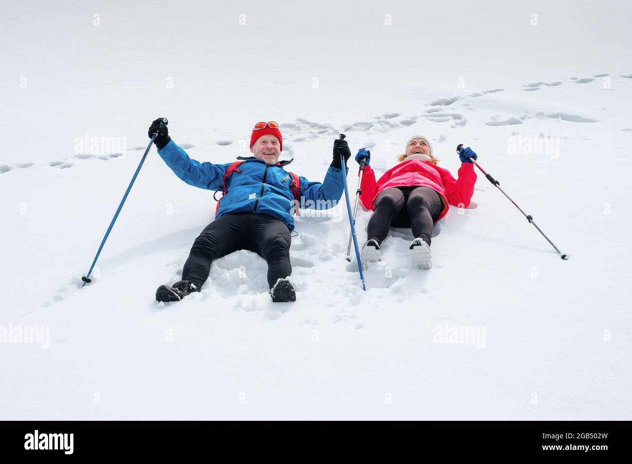 Lächelndes Senioren-Paar, das draußen auf Schnee liegt und fröhlich lacht. Stockfoto