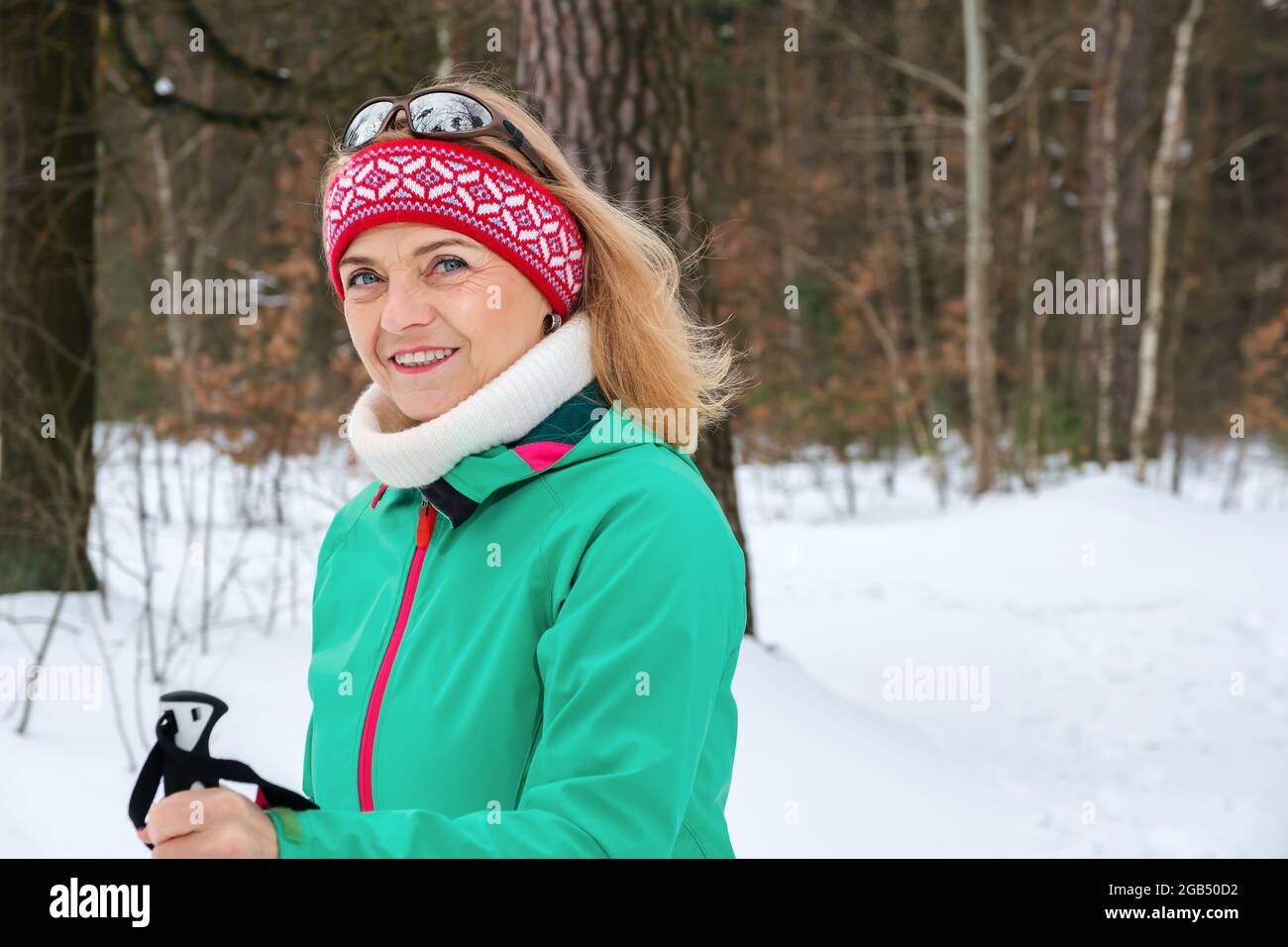 Porträt einer älteren Frau, die mit Nordic-Walking-Stöcken im Winterwald steht Stockfoto