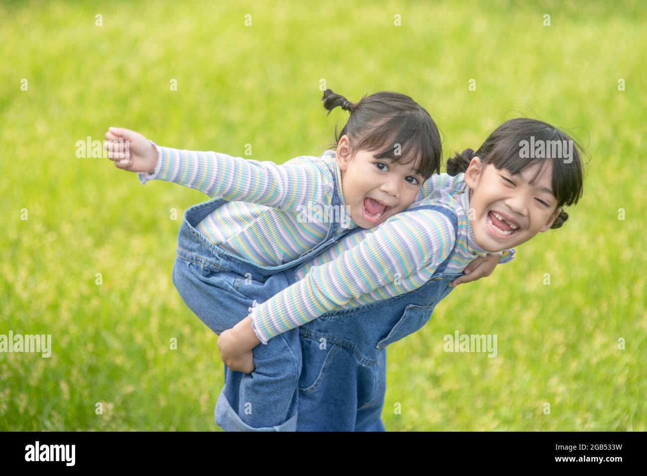 Asiatisches kleines Mädchen mit älterer Schwester in einem Park, der auf ihrem Rücken reitet Stockfoto