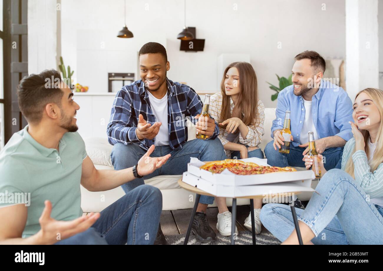 Eine Gruppe internationaler Freundinnen und Freundinnen, die zu Hause Pizza essen und Bier trinken Stockfoto