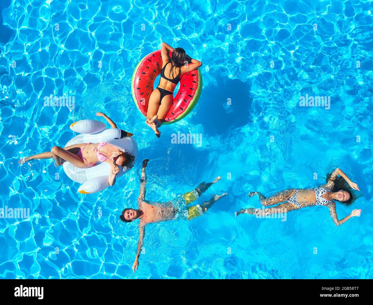 Antenne von Freunden, die Party im Schwimmbad mit aufblasbaren Flamingo, Schwan, Matratzen. Glückliche junge Leute entspannen im Luxus-Resort an sonnigen Tag. Vi Stockfoto