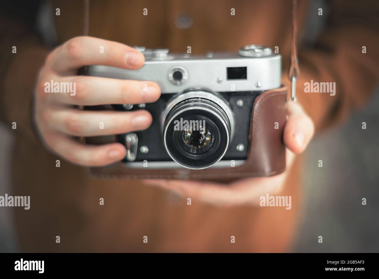 Fotograf in brauner Jacke, der die Retro-Kamera aus der Nähe in die Hände nimmt Stockfoto