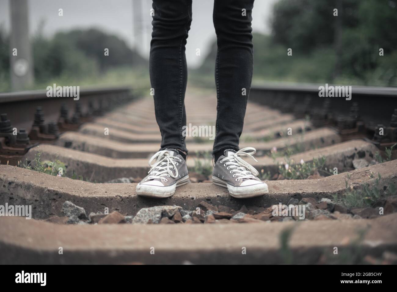 Hipster-Mann in schwarzer Jeans-Hose und grauen Sneakers auf der Bahn Stockfoto