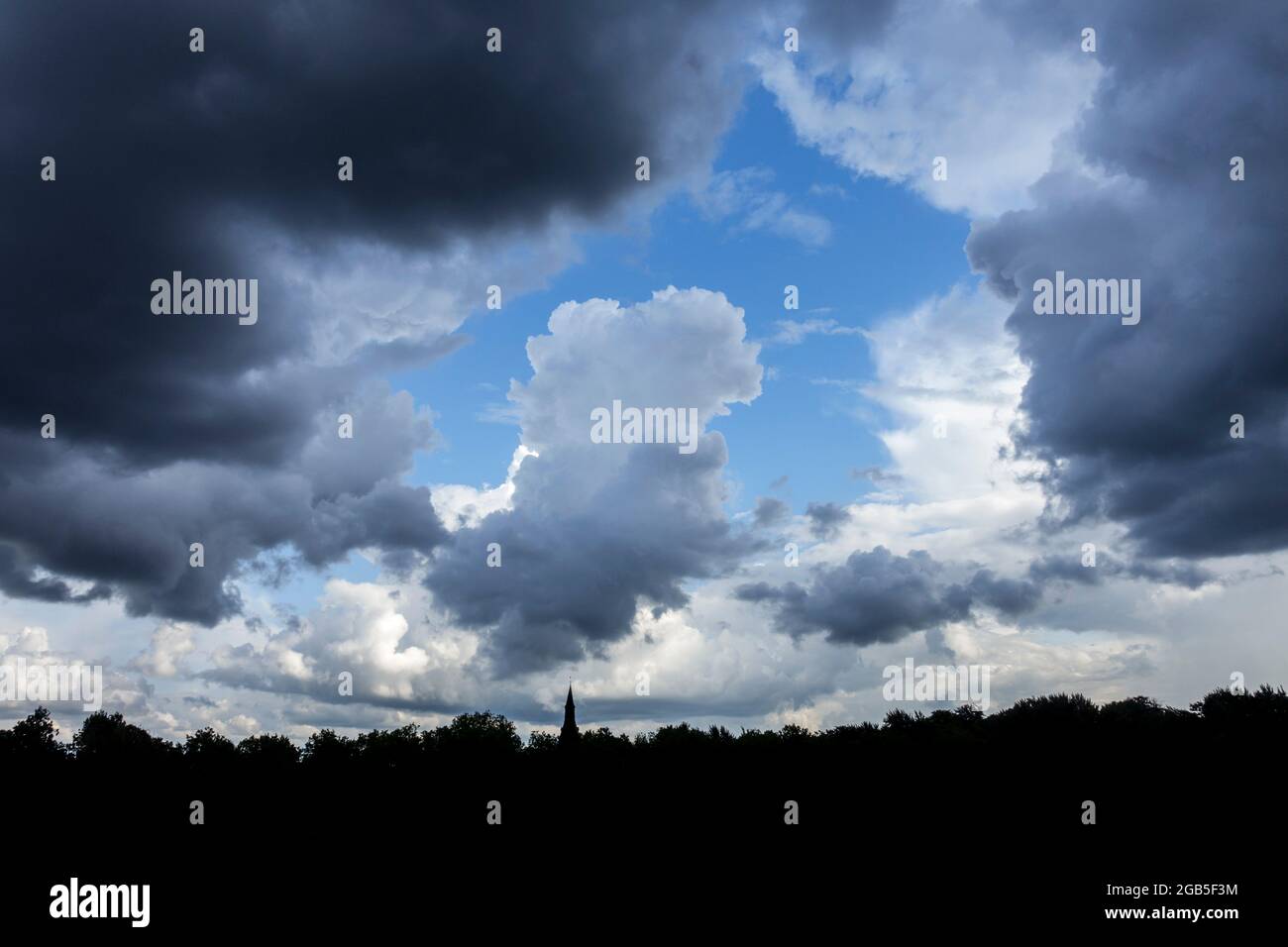 Lücke in weißen und grauen Cumuluswolken, die an einem regnerischen Sommertag einen blauen Himmel zeigen Stockfoto