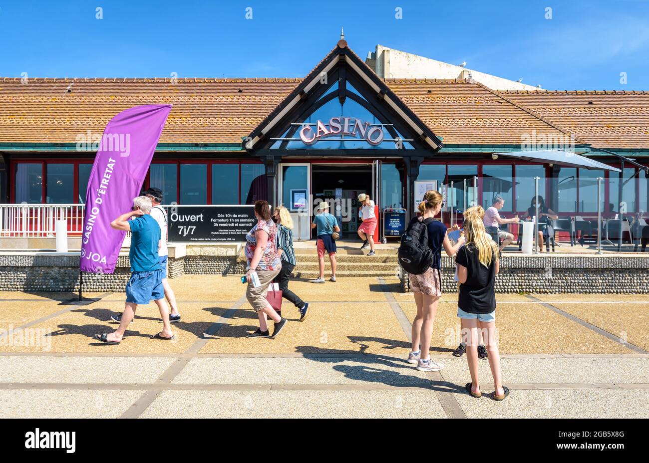 Touristen bummeln in der Familie oder zwischen Freunden entlang der Strandpromenade in Etretat, Frankreich, und gehen an einem sonnigen Tag am Eingang des Casinos vorbei. Stockfoto