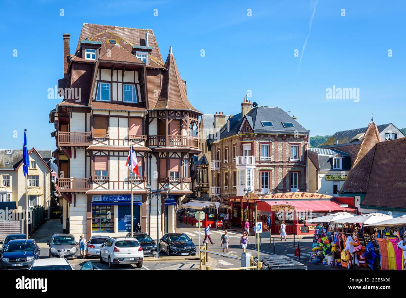 Typische normannische Gebäude auf dem Victor Hugo Platz in Etretat, Frankreich, mit Straßencafés, Restaurant und einem Strandgeschäft an einem sonnigen Tag. Stockfoto