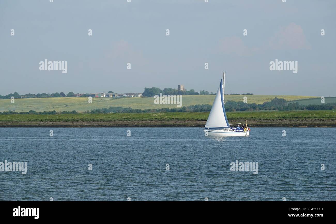 NORTH FAMBRIDGE, VEREINIGTES KÖNIGREICH - 06. Jun 2021: Ein Segelboot auf dem Fluss Crouch in Essex mit der Canewdon-Kirche am Horizont. Stockfoto