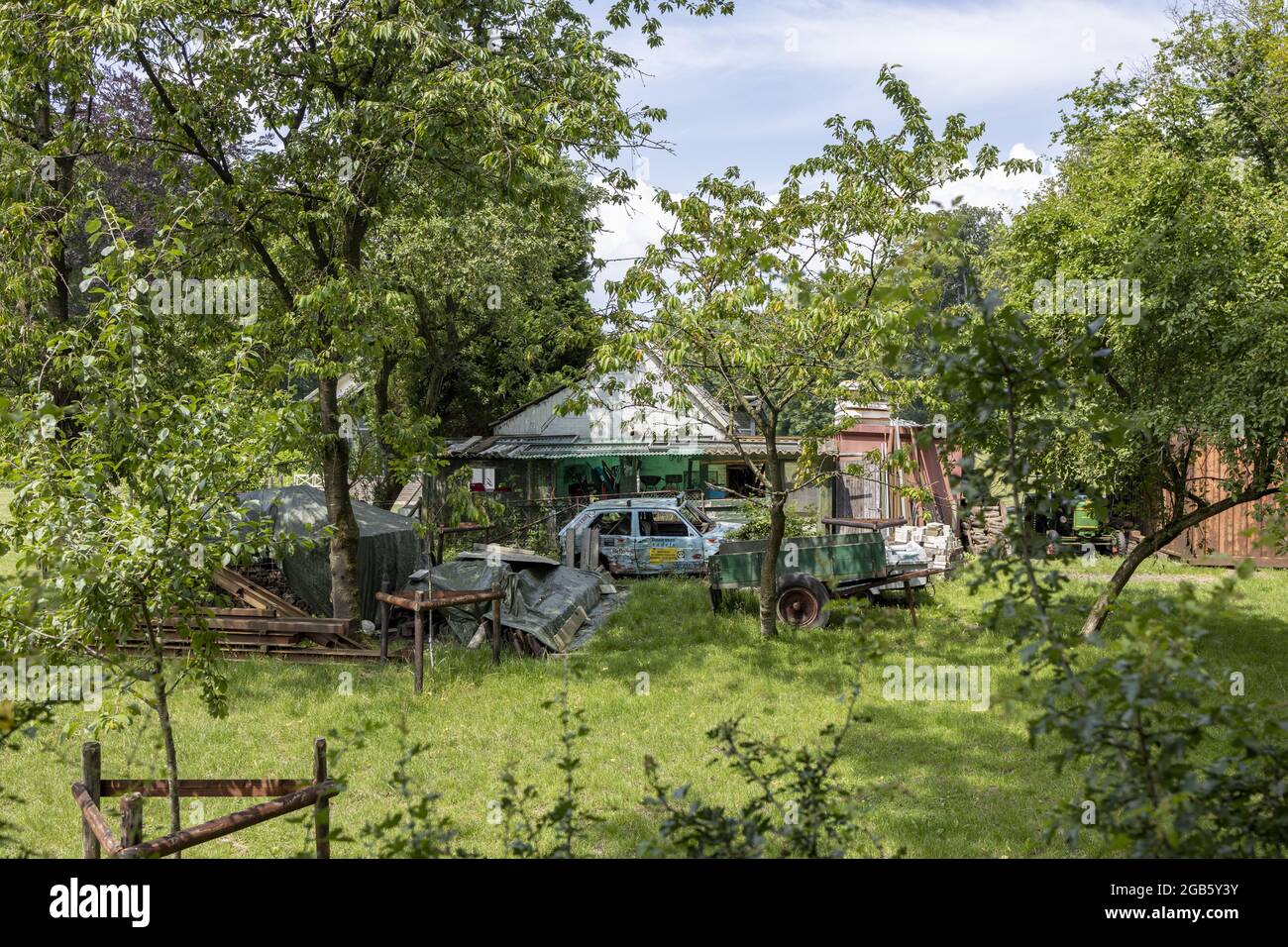 ZUTPHEN, NIEDERLANDE - 20. Jun 2021: Lebhafter grüner Garten mit Bäumen und alten Rennwagen mit Logos, die vor einem Schuppen mit anderen ma geparkt sind Stockfoto