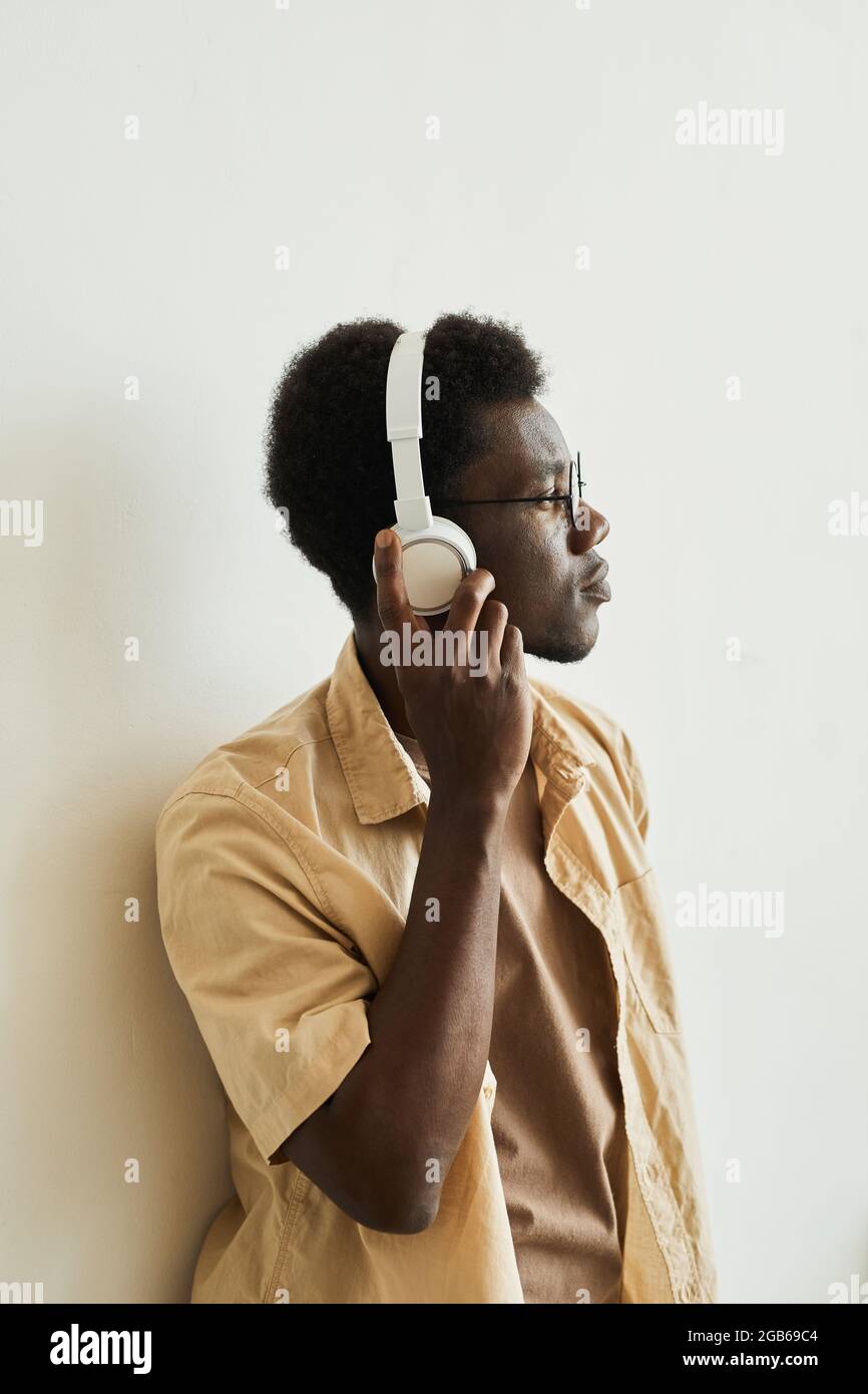 Afrikanischer junger Mann, der kabellose Kopfhörer aufsetzt, um Musik auf weißem Hintergrund zu hören Stockfoto