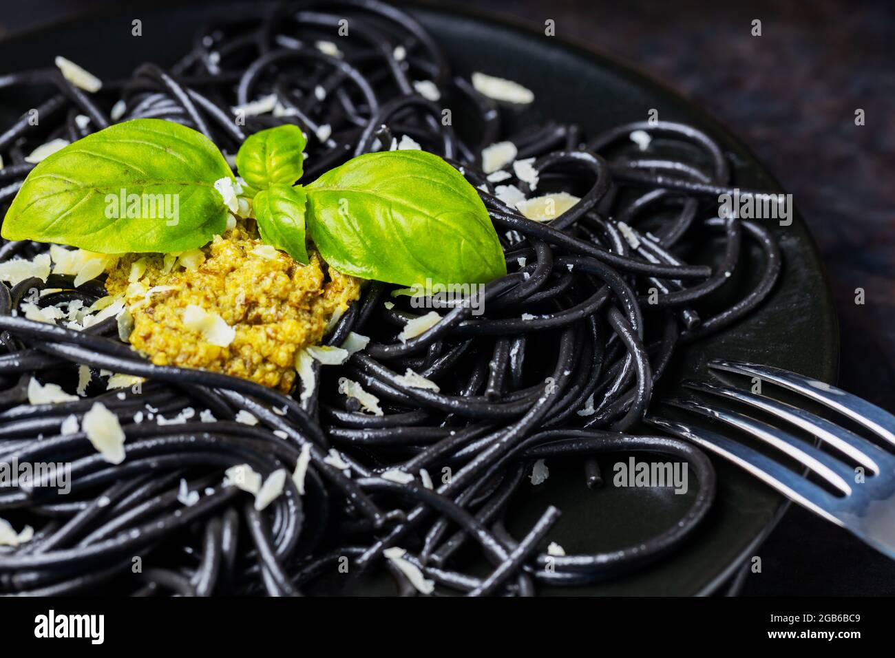 schwarze-pasta-tintenfisch-tinte-mit-sosse-pesto-und-frischem-basilikum-schwarze-spaghetti-mit-basilikumblattern-auf-schwarzem-teller-dunkler-hintergrund-2gb6bc9.jpg