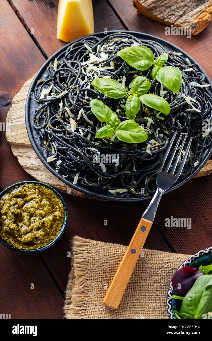 Pasta-Spaghetti mit Parmesankäse, Basilikum und Pesto-Sauce. Schwarze Pasta, Saucenpesto und frisch gemischter Salat aus Grüns auf Holzbrettern. Flach liegend. Oben vi Stockfoto