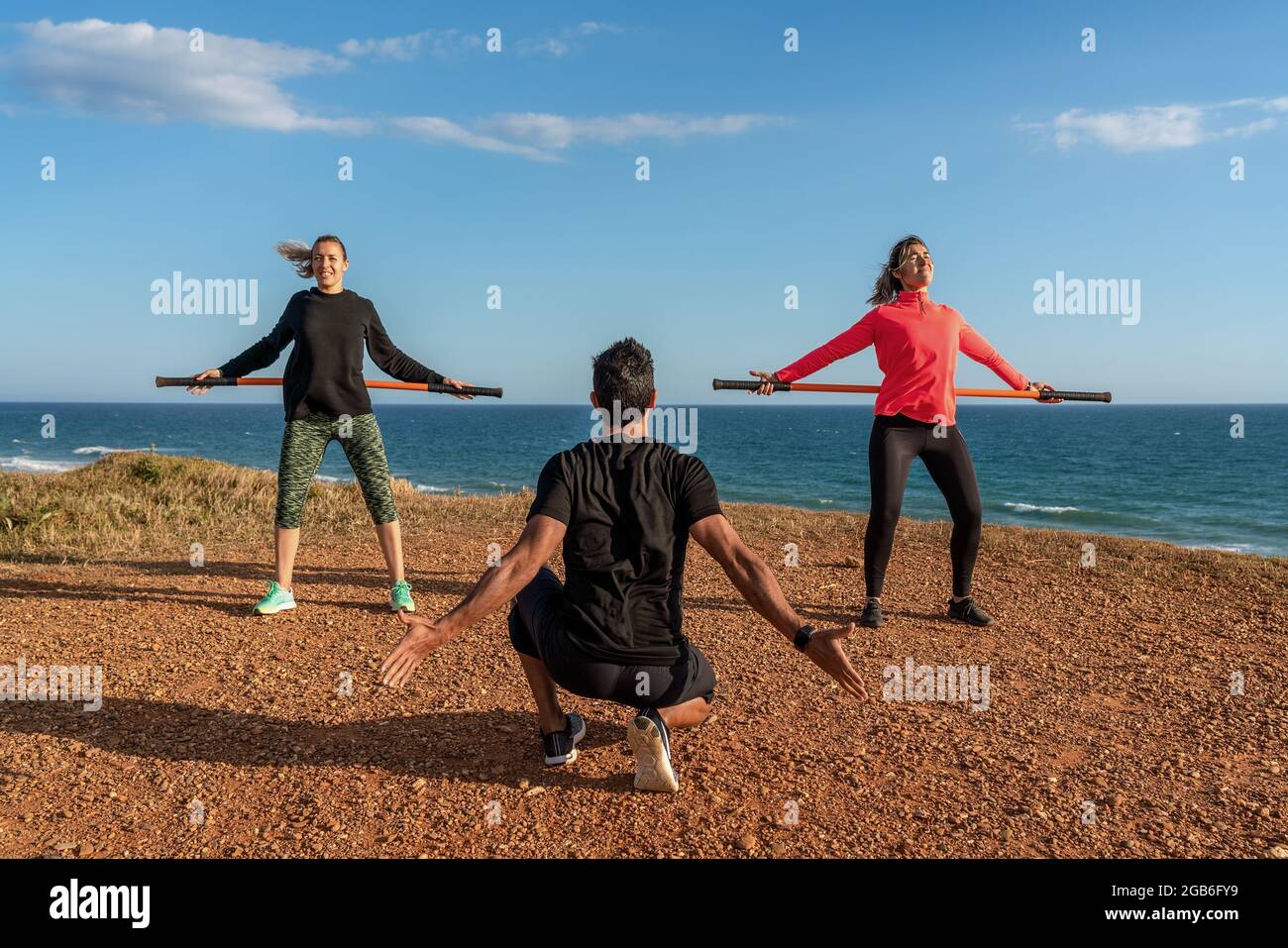 Ein Mann und eine Frau im mittleren Alter führen an der Küste Fitnesskurse durch. Verwenden von Gymnastikstäben zum Dehnen. Blauer Himmel. Stockfoto