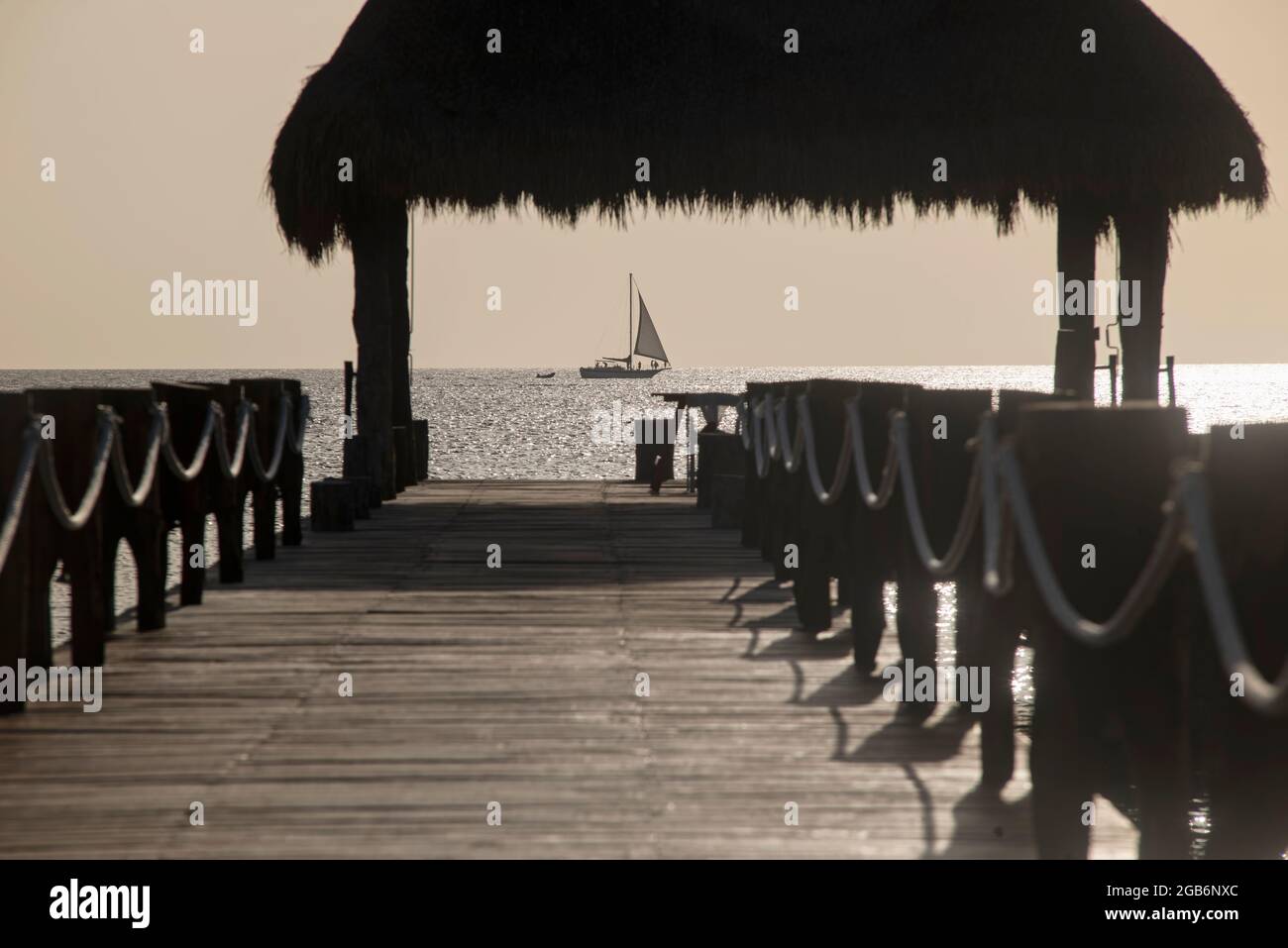 Hölzerner Pier auf dem Meer gegen das Licht mit einem Segelboot am Horizont, die tropische Insel Cozumel in Mexiko. Selektiver Fokus. Stockfoto