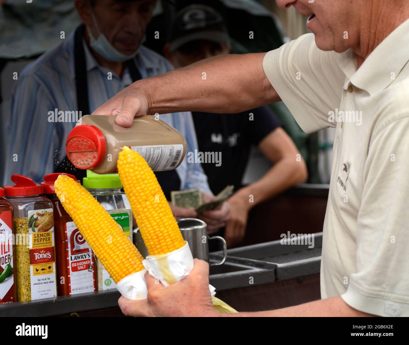 Ein Mann kauft zwei Ähren geröstetem Mais auf dem Cob an einem Lebensmittelstand in Santa Fe, New Mexico. Stockfoto