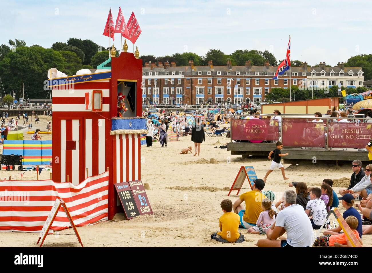 Weymouth, England - 2021. Juli: Menschen, die am Strand sitzen und eine Aufführung von traditionellem Punch und Judy beobachten Stockfoto