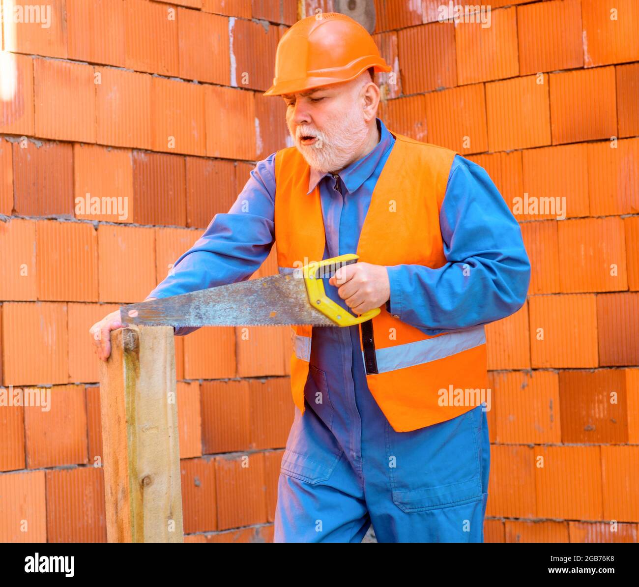 Zimmermann auf der Baustelle schneidet Holz mit Säge. Professioneller Arbeiter in Hut und Overalls. Stockfoto