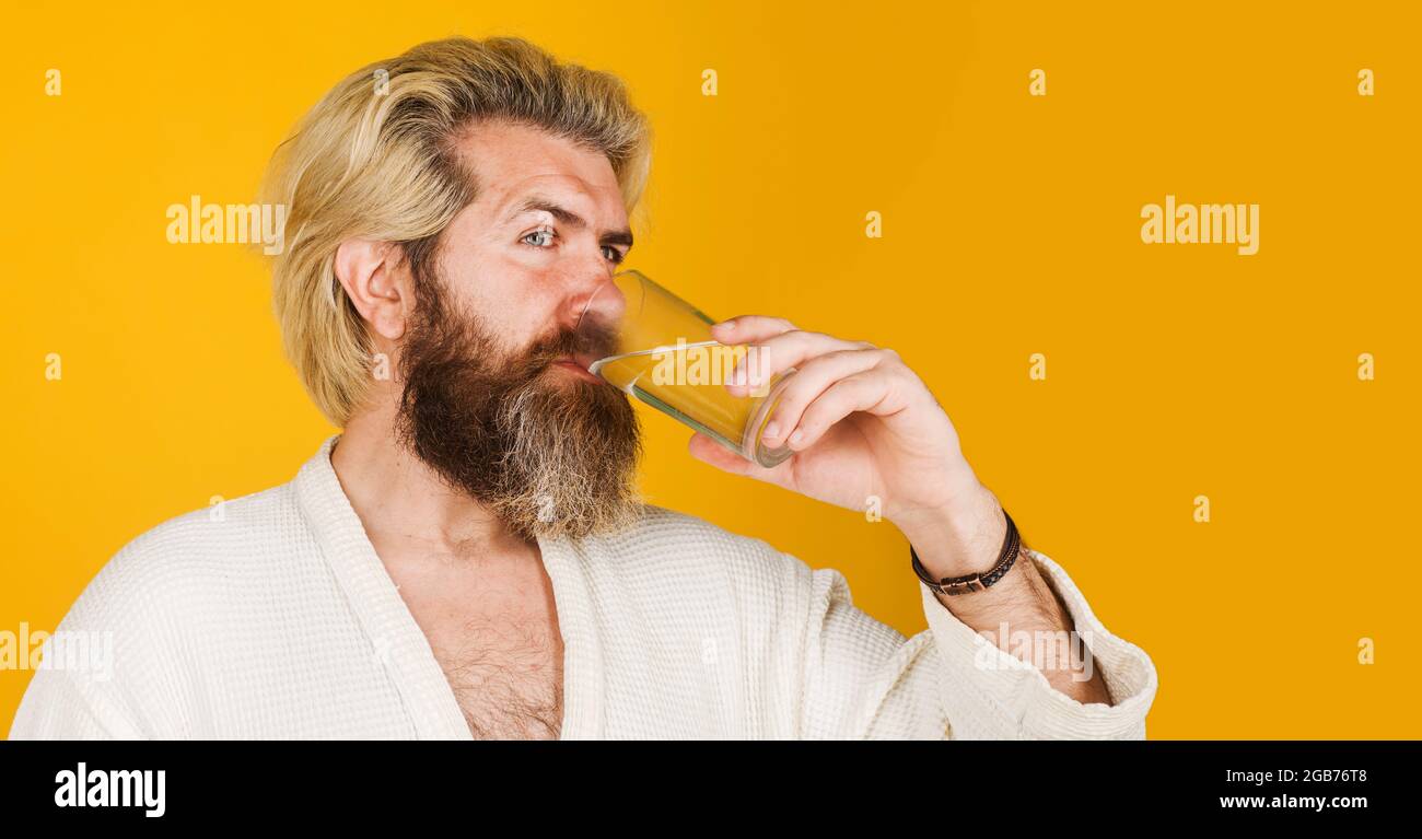 Bärtiger Mann mit einem Glas Wasser. Mann im Bademantel, der morgens Mineralwasser trinkt. Gesunde Ernährung. Stockfoto