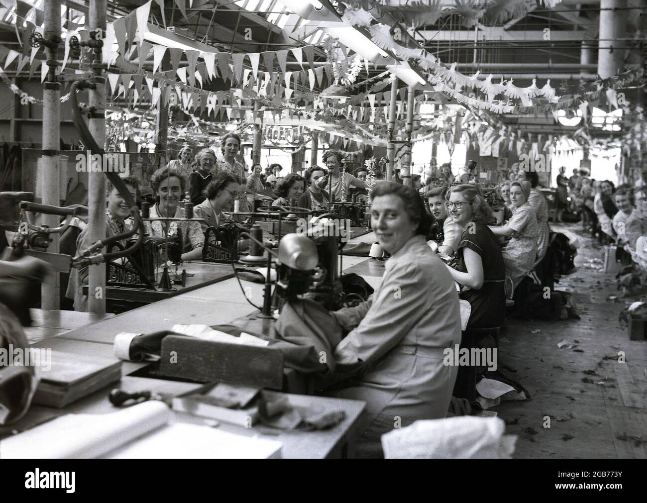 1953, historisch, Arbeiterinnen, Streams, in der Fabrik des berühmten Bekleidungsherstellers Hepworths, sitzend für ein Bild, einige tragen kleine Partyhüte und mit einer Verhängung zur Krönung der Königin, die vom Dach des Providence Works auf der Claypit Lane, Leeds, England, Großbritannien, hängt. Hepworth’s wurde von Joseph Hepworth gegründet, dem Sohn eines ‘„Tuchkleiders“ aus Lindley in der Nähe von Huddersfield, der noch als Schuljunge in die Fußstapfen seines Vaters trat und in Teilzeit in einer lokalen Fabrik zu Wollkleidern wurde. 1914 war Joseph Hepworth & Son wahrscheinlich der größte Bekleidungsmann Stockfoto