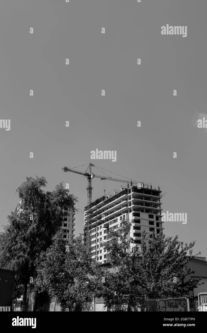 Schwarz-Weiß-Foto eines mehrstöckigen Wohngebäudes im Bau und Kran auf einem Hintergrund des blauen Himmels Stockfoto
