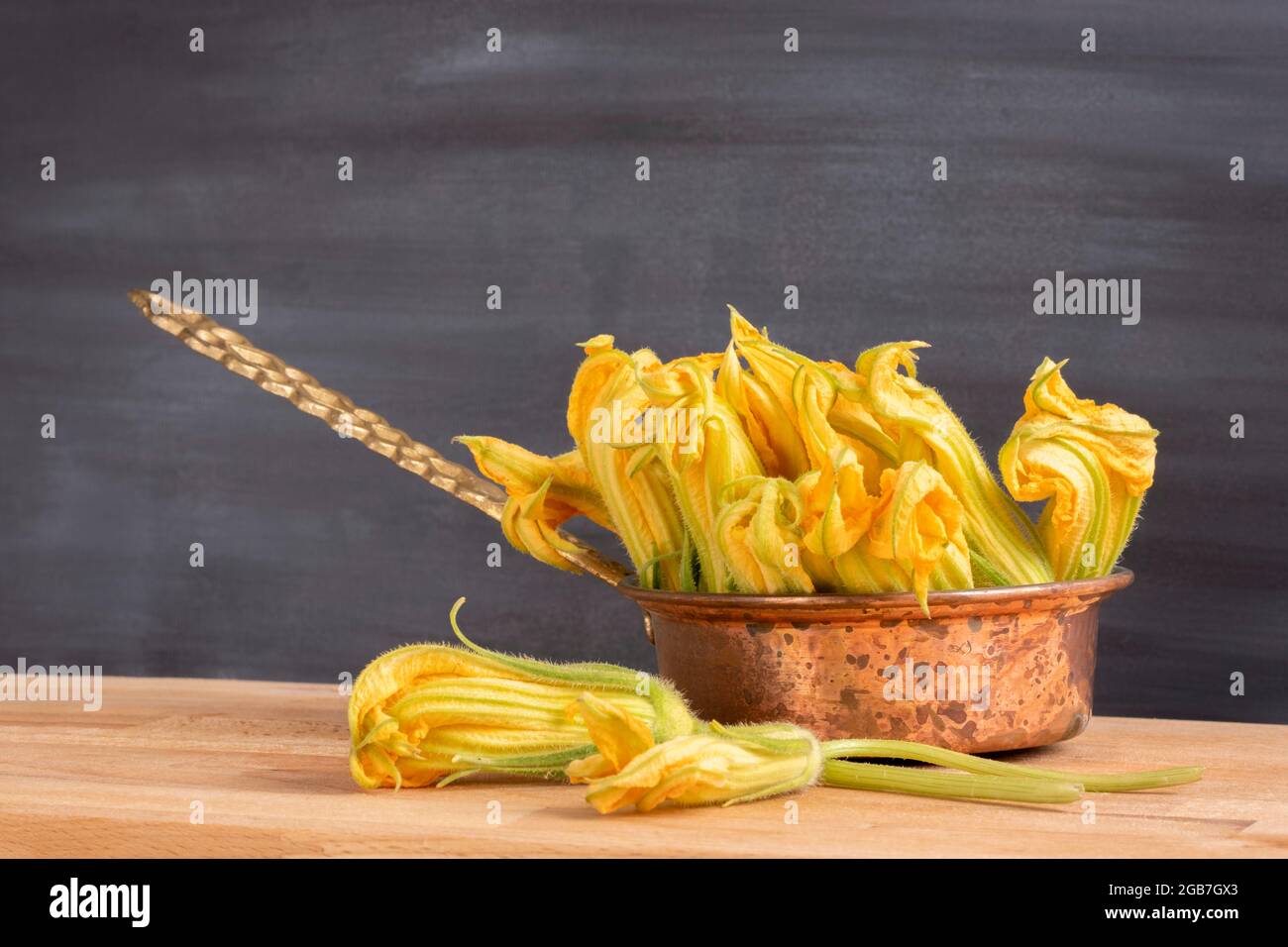 Rohes, essbares Zucchini-Blumenkonzept: Bio- und frische gelbe Kürbisblüten im Kupfertopf. Gesunde Lebensweise Zutat. Mediterrane Küche Stockfoto