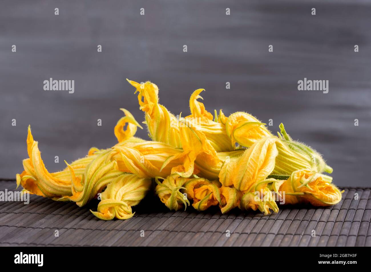 Konzept der rohen Zucchini-Blumen:feine Küche mit essbaren frischen und biologischen Blumen. Zutaten für einen gesunden Lebensstil. Gelbes Gemüse auf schwarzem Hintergrund Stockfoto