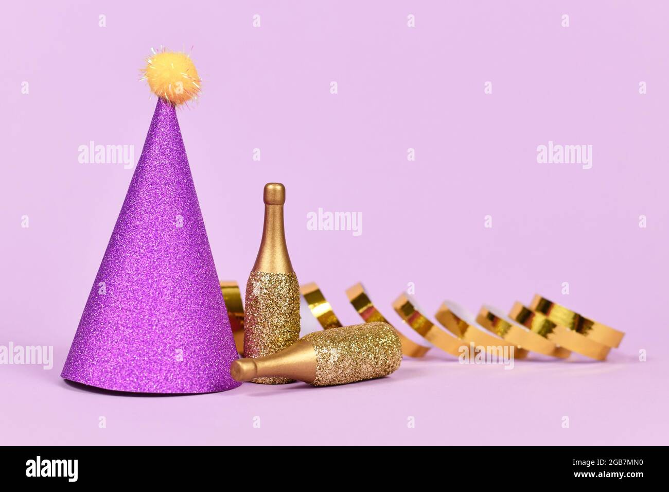 Partyhut, kleine goldene Champagnerflaschen und Partystreamer auf violettem Hintergrund mit Kopierfläche Stockfoto