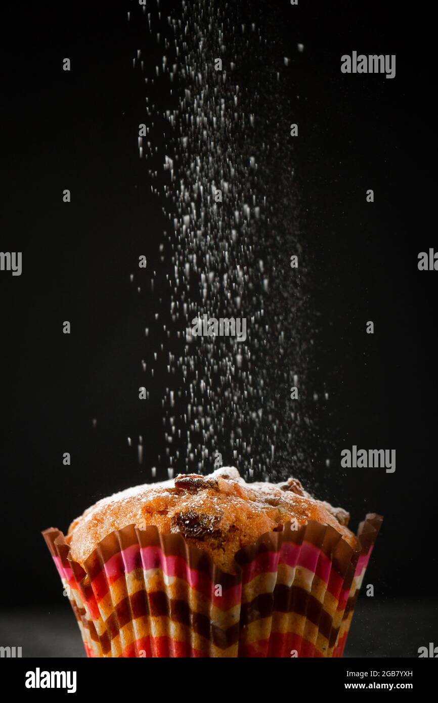 Leckerer Muffin in Puderzucker auf schwarzem Hintergrund. Der Prozess der Herstellung von hausgemachtem Kuchen. Vertikales Foto. Stockfoto