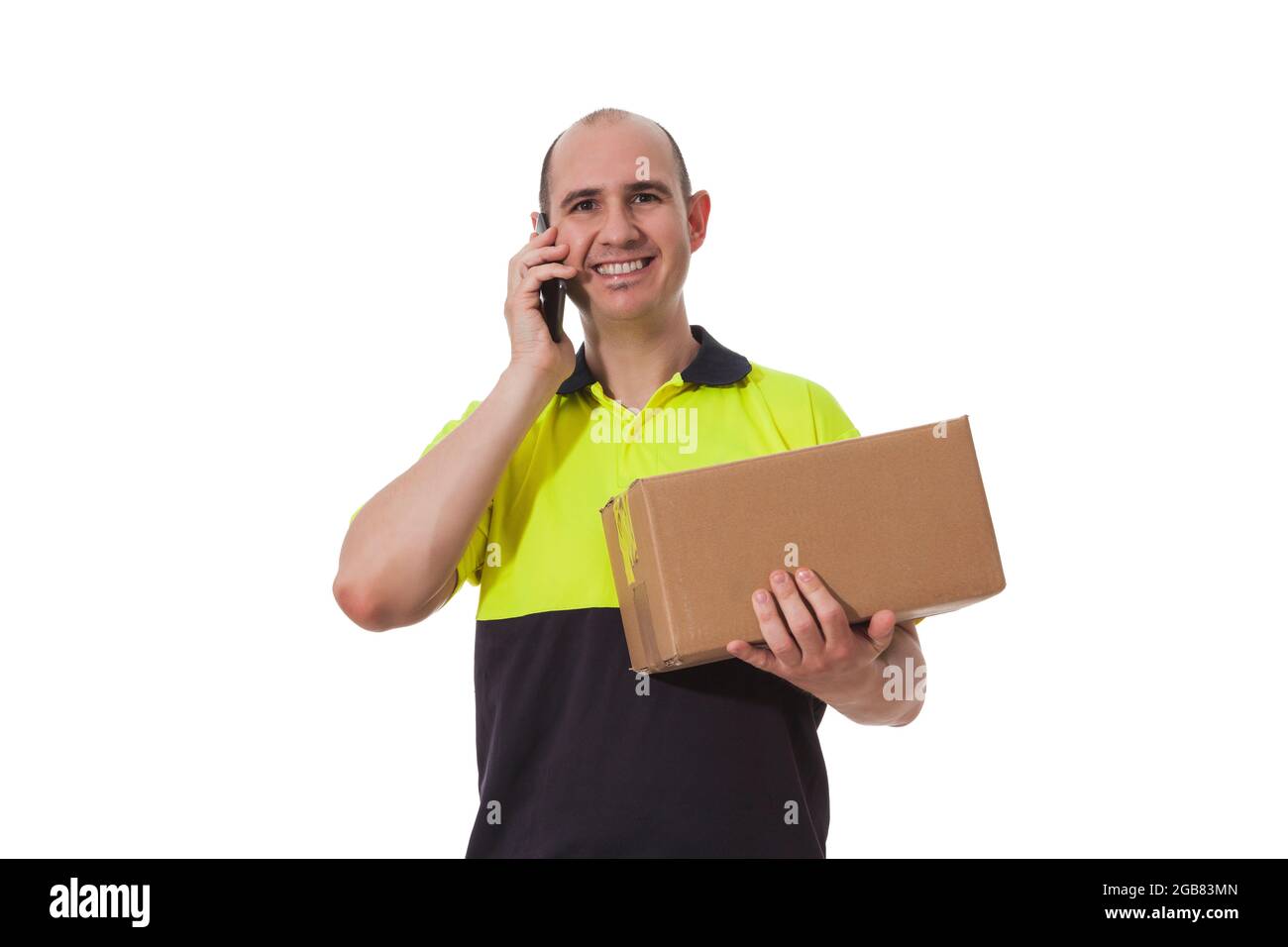 Ein lächelnder, kahler Kaukasusmann hält mit seinem linken Arm einen Karton, während er mit seiner rechten Hand sein Mobiltelefon neben sein Ohr hält, während er m ist Stockfoto