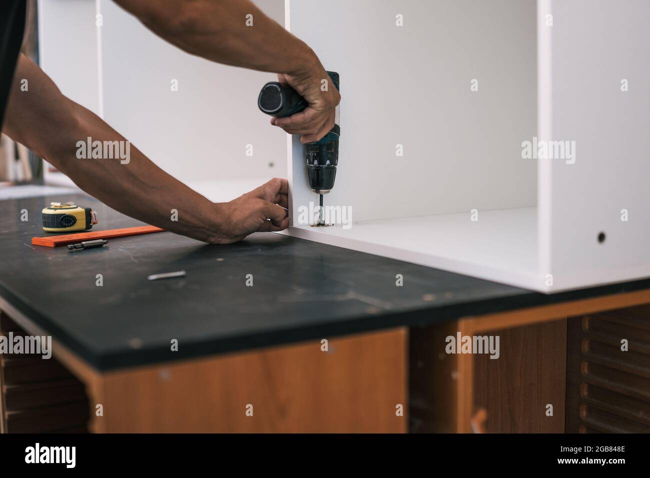 Hände nageln eine Schraube mit einem Bohrer in ein weißes Holzmöbel Stockfoto