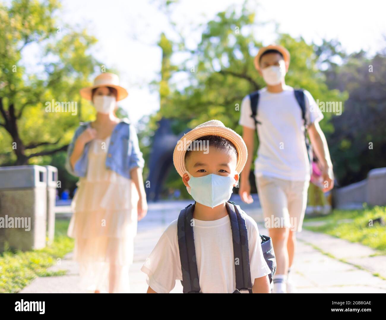 Glückliche Familie, die die medizinische Maske trägt und im Park spazierengeht. Familienurlaub während der Coronavirus-Covid-19-Pandemie. Stockfoto