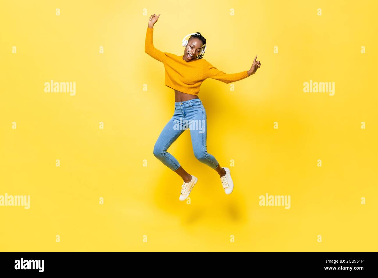 Springendes Porträt einer glücklichen, energiegeladenen jungen afroamerikanischen Frau, die Kopfhörer trägt und Musik auf gelbem, isoliertem Studiohintergrund hört Stockfoto