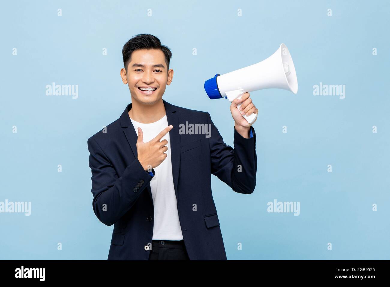 Lächelnd schöner asiatischer Mann hält Megaphon in hellblau isoliert Hintergrund Stockfoto