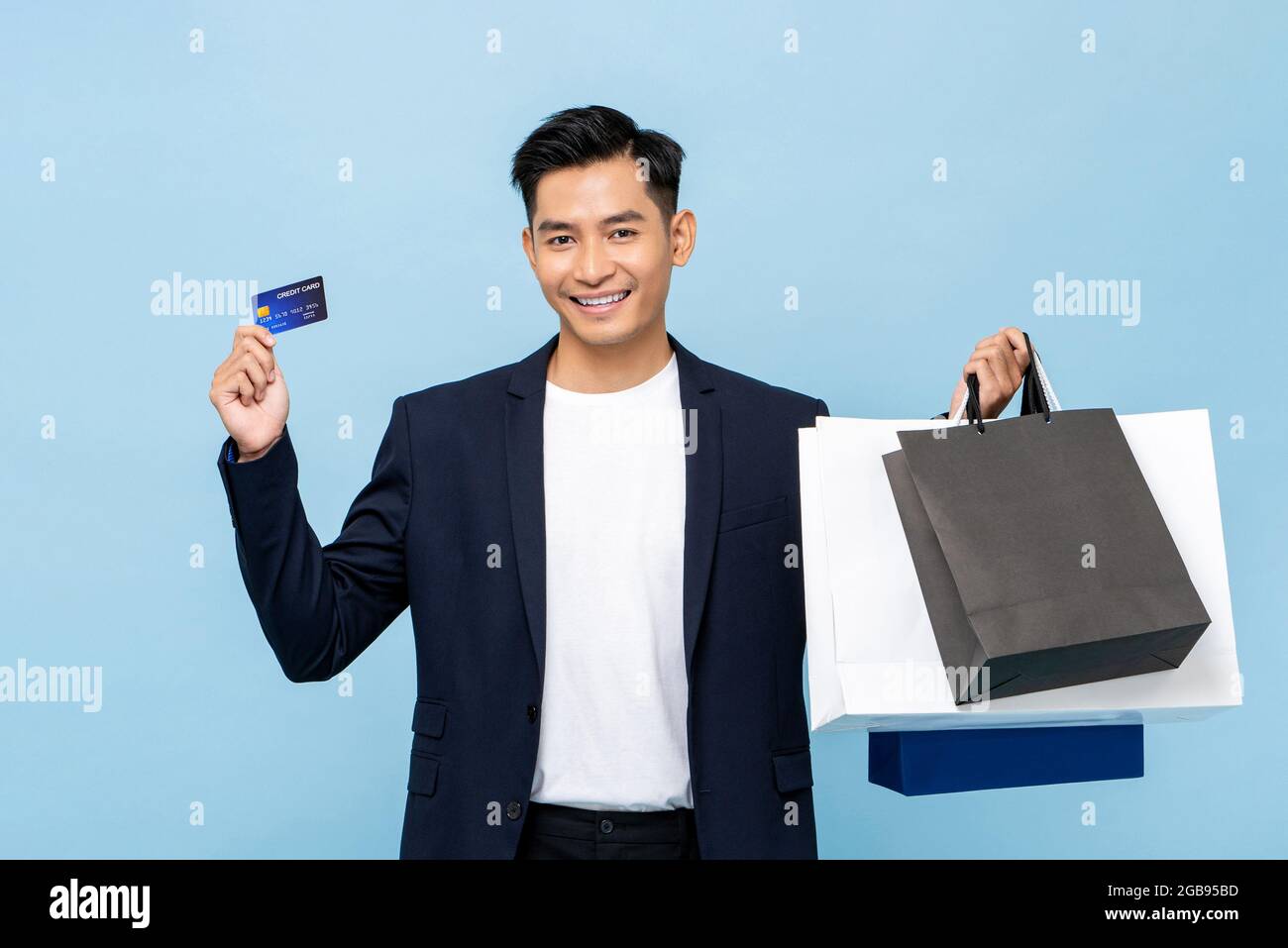 Junger gutaussehender Mann aus Südostasien mit Kreditkarte und Taschen in hellblauem, isoliertem Studio-Hintergrund für bargeldloses Shopping-Konzept Stockfoto