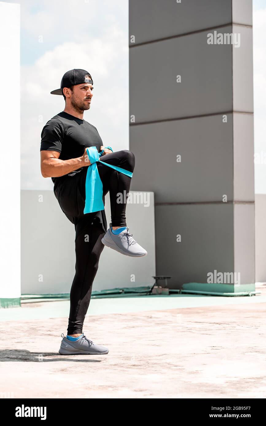 Handsome hispanischen Mann Aufwärmen mit elastischen Widerstandsband vor Trainieren Sie im Freien auf dem Dach - zu Hause Open Air trainieren Konzept Stockfoto