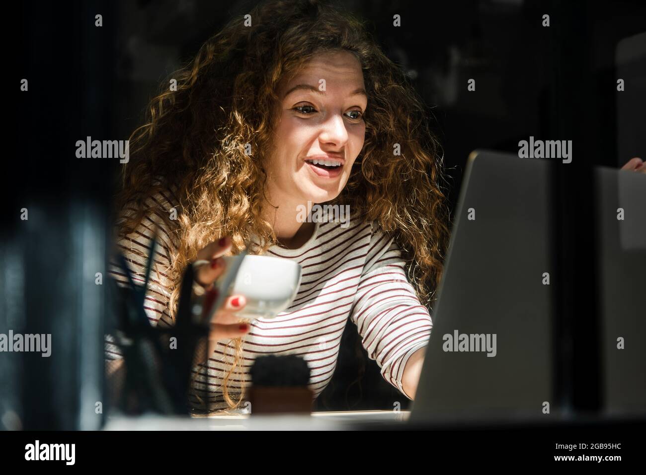 Fröhliche, lächelnde kaukasische Frau mit Kaffee, die am frühen Morgen zu Hause einen Laptop-Computer ansah, der bei einem Videoanruf sprach Stockfoto