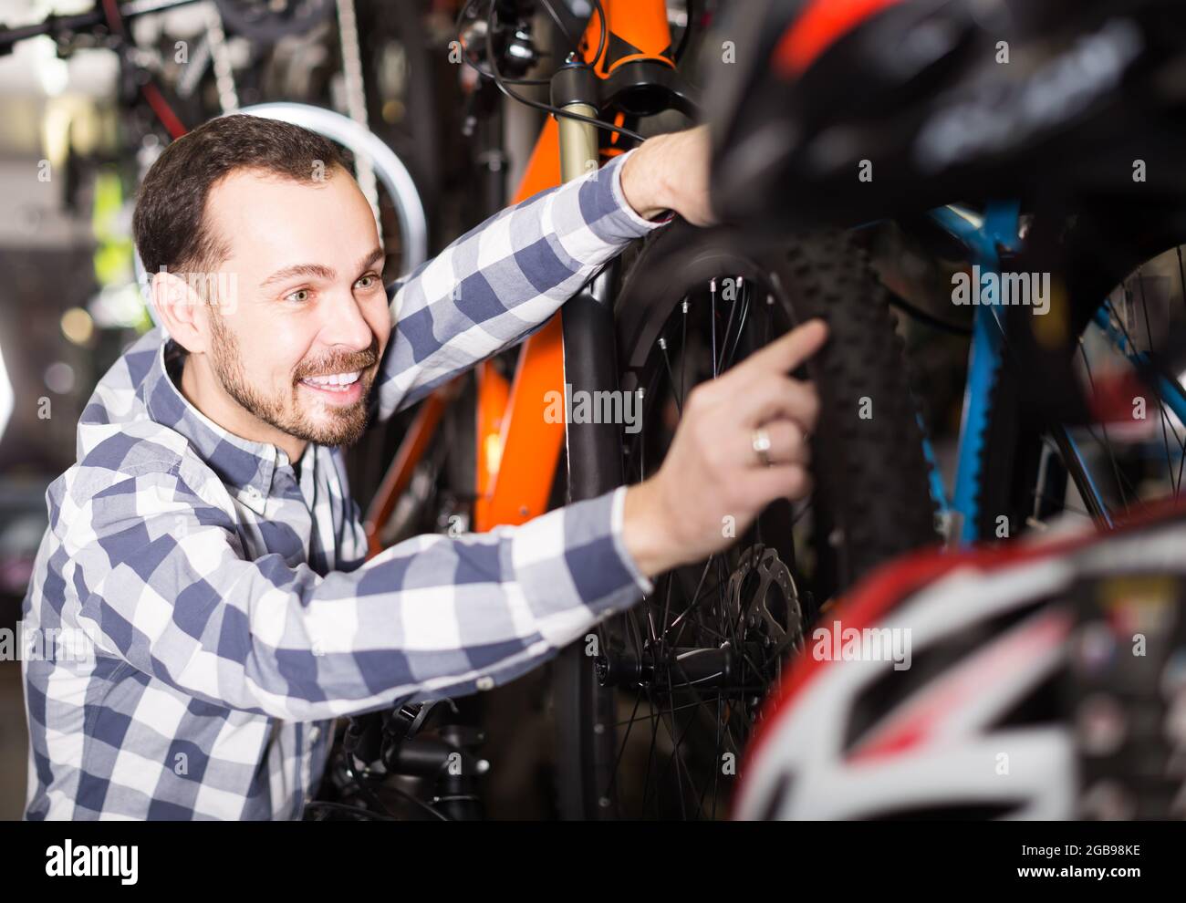 Fröhlicher Mann im Sportgeschäft behandelt Fahrräder und weist auf interessante Details hin Stockfoto