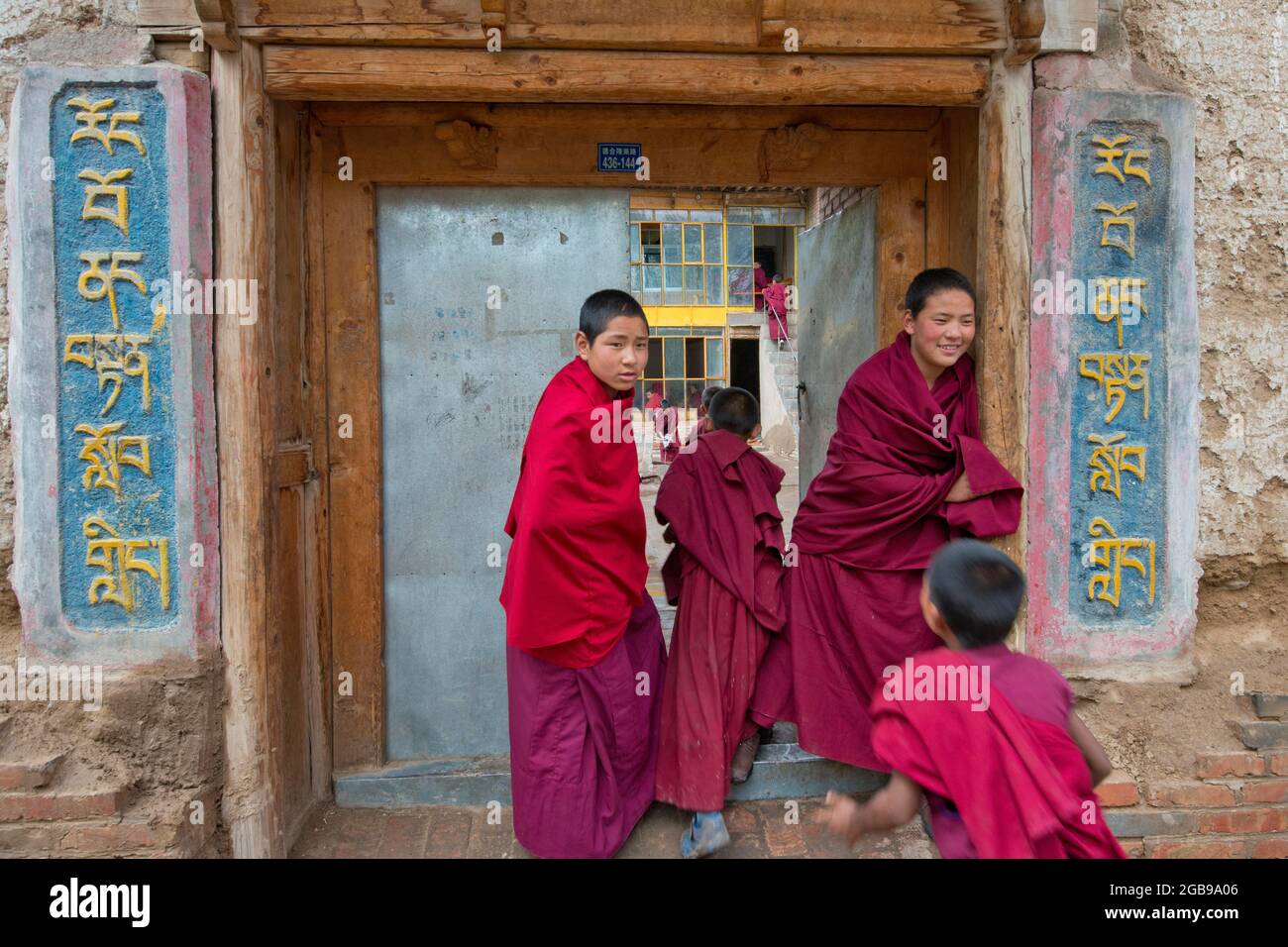 Junge Novizen, Mönchskülern vor dem Eingang zur buddhistischen Klosterschule, Klostergebäude im traditionellen Architekturstil, Tongren Stockfoto