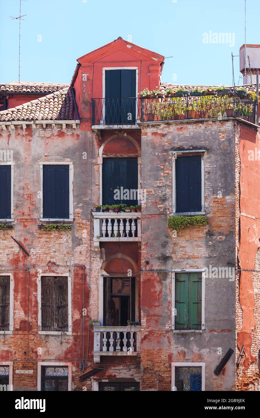 Altes venezianisches Gebäude mit verfallenen roten Backsteinwänden. Geschlossene Fensterläden Stockfoto