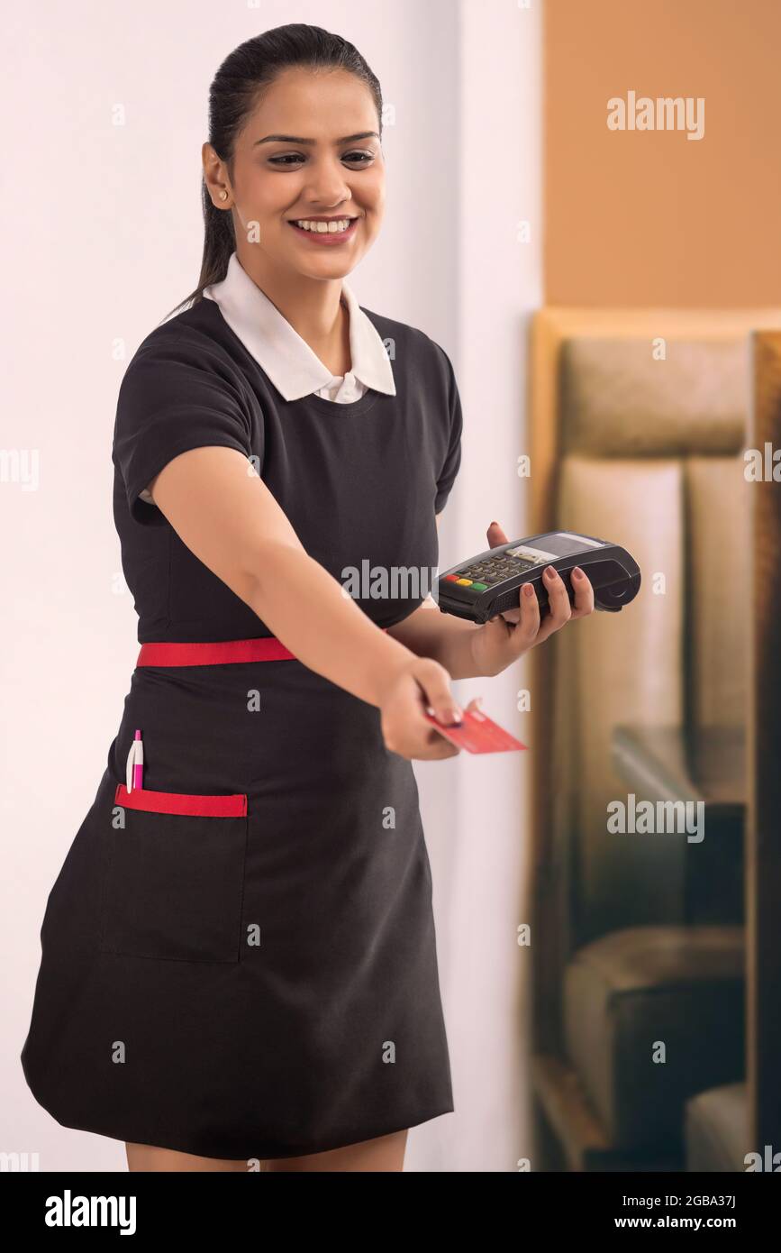 EINE FRÖHLICHE KELLNERIN, DIE IHRE DEBITKARTE NACH DER ZAHLUNG ZURÜCKGIBT Stockfoto
