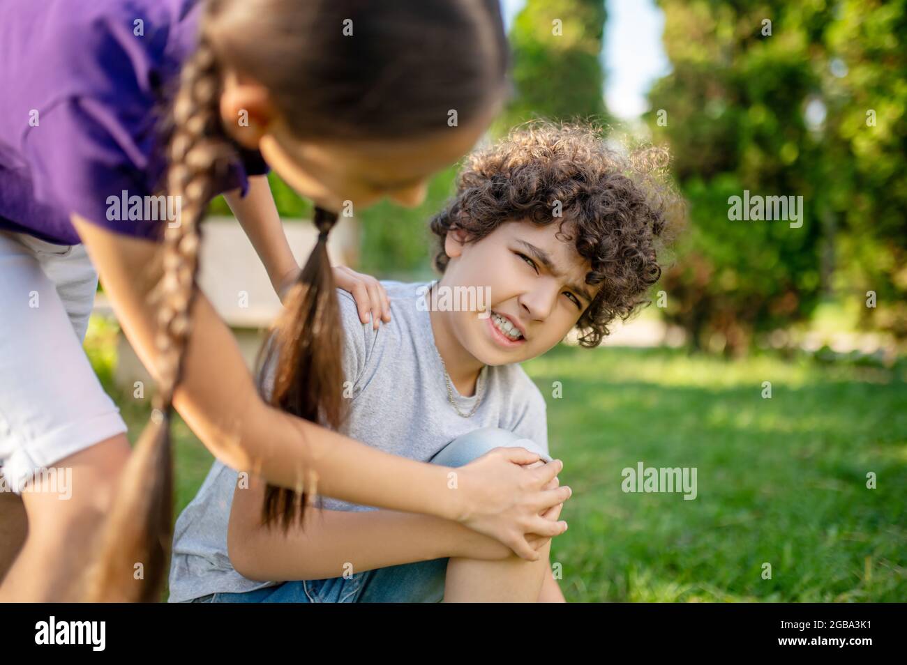 Junge mit Grimasse berühren sein Knie und Freundin Stockfoto