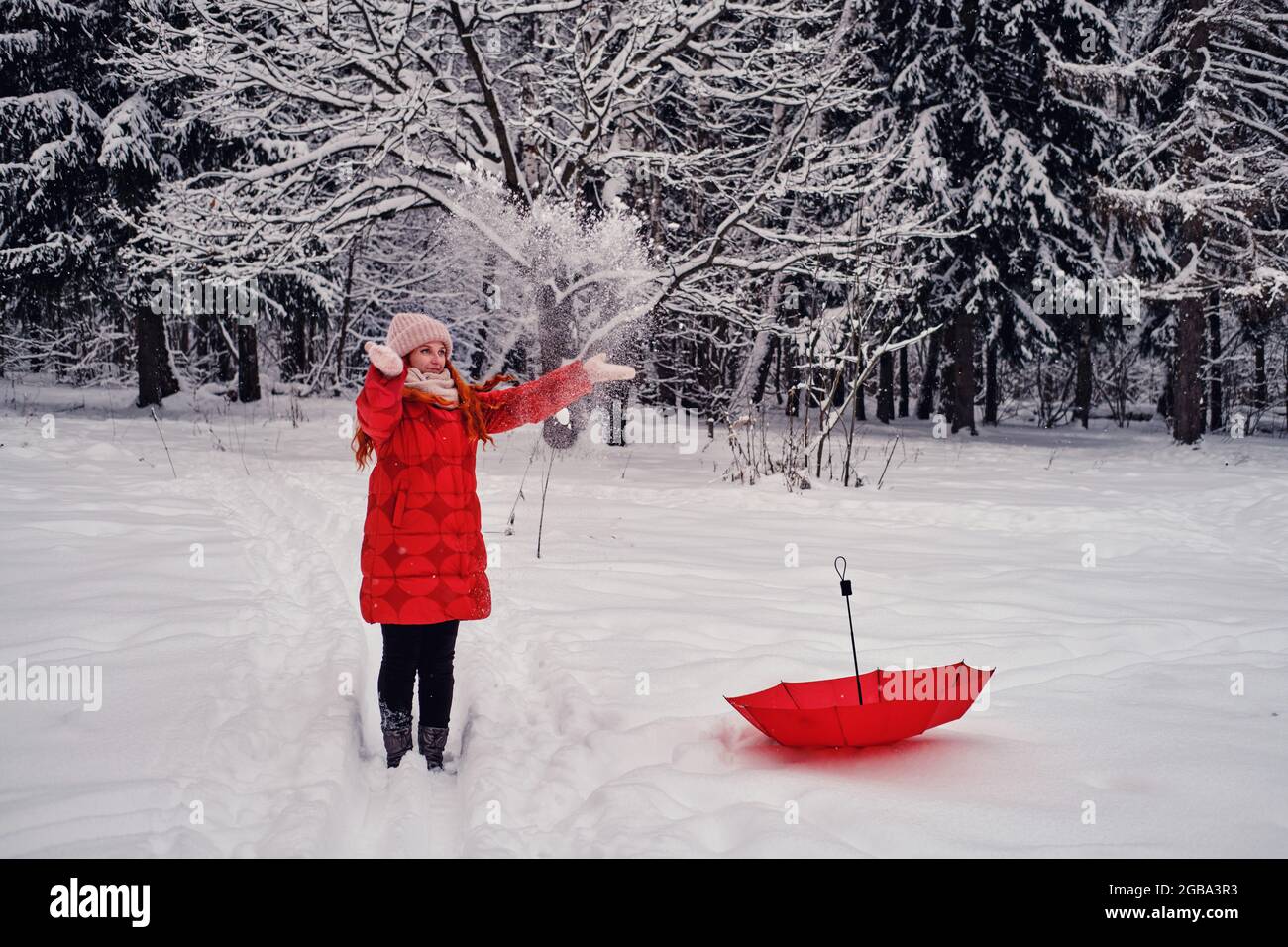 Eine lächelnde Frau wirft Schnee mit ihren Händen, einen Winterwald mit gefrorenen Bäumen Stockfoto