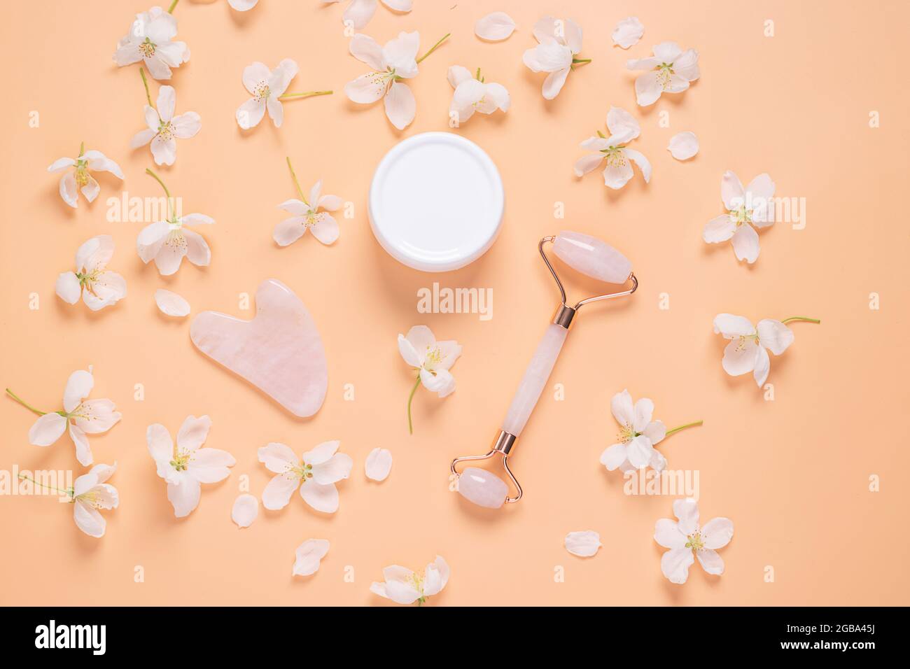 Gesichtsmassage-Set Roller Scraper guasha kosmetisches Öl Serum Gesichtspflege auf pastellrosa Hintergrund Stockfoto