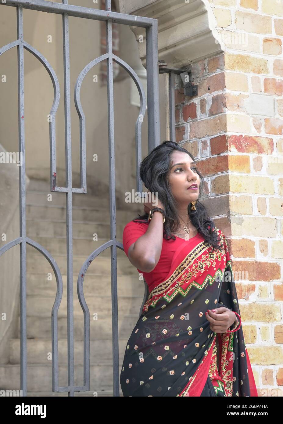 Wunderschöne indische Frau mit rotem Saree, die vor einer Tür neben einer Backsteinmauer steht. Speicherplatz kopieren. Stockfoto