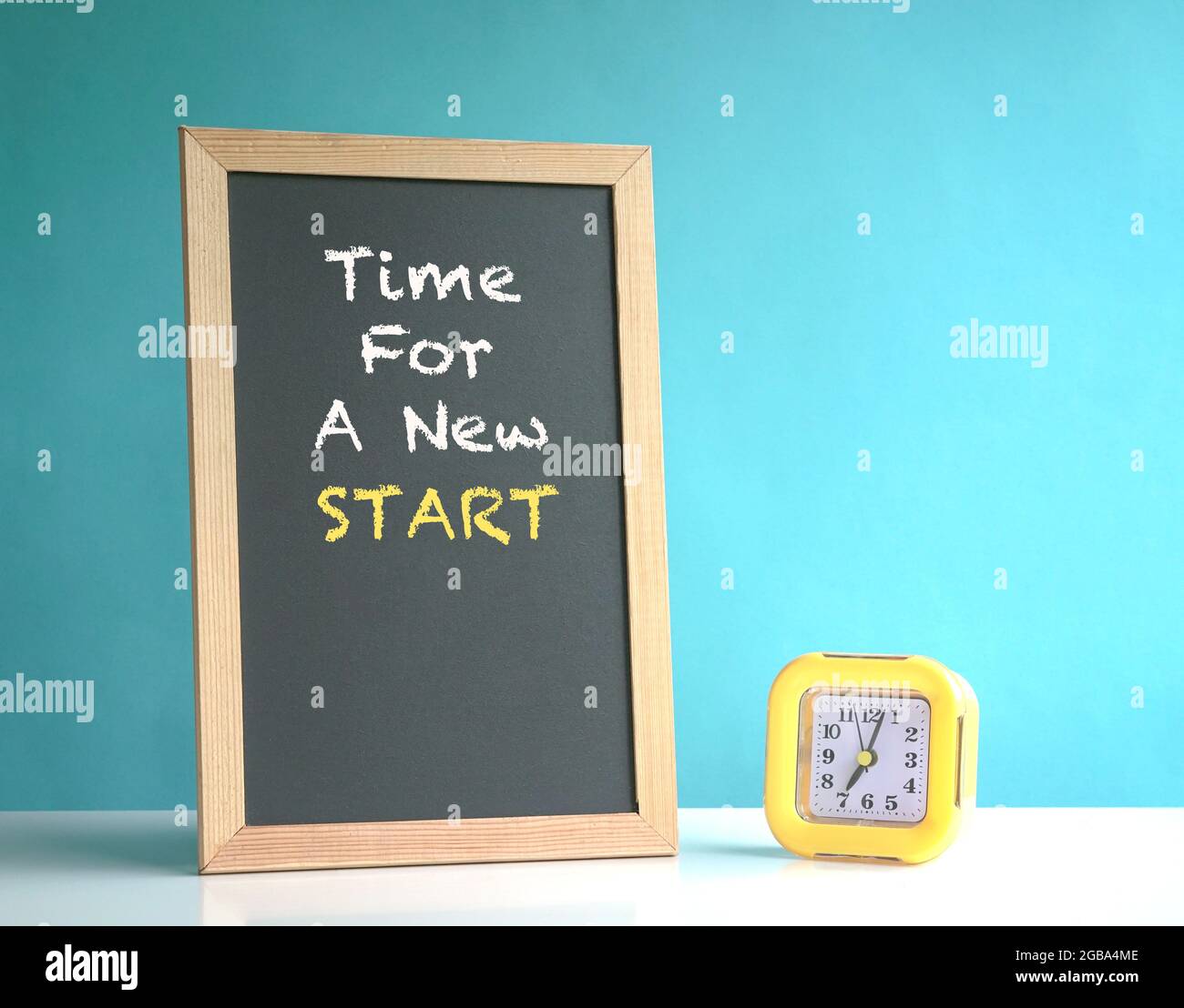 Zeit für einen neuen Start, Phrase an der Tafel. Neben einem gelben Wecker. Auf blauem Hintergrund. Stockfoto